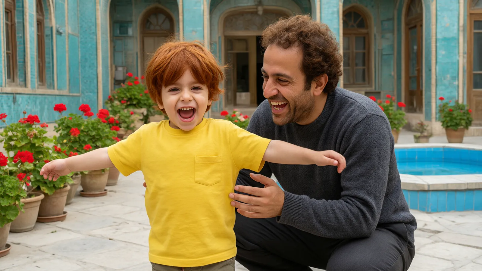 پسر سه‌ساله با تیشرت زرد در حیاط کاشی فیروزه‌ای با شادی می‌چرخد و پدر با پلیور خاکستری می‌خندد